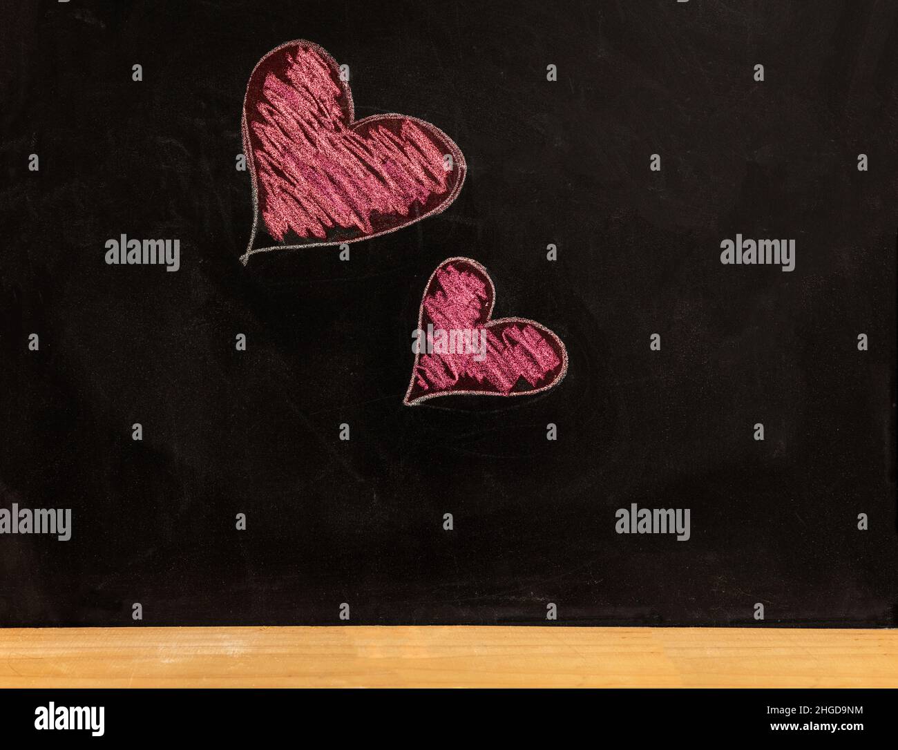 Dessin de coeur sur le tableau noir de l'école.Amour, symbole de Saint-Valentin.Deux coeurs rouges, petits et grands, dessinés à la main sur un tableau noir Banque D'Images