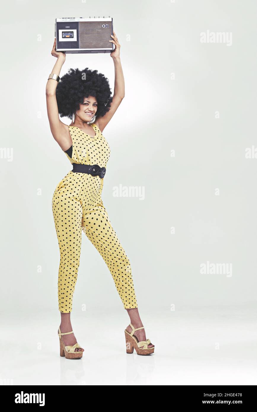Sentir la 70s Vibe.Une jeune femme portant une combinaison rétro 70s tenant un lecteur de cassettes et frappant une pose disco. Banque D'Images