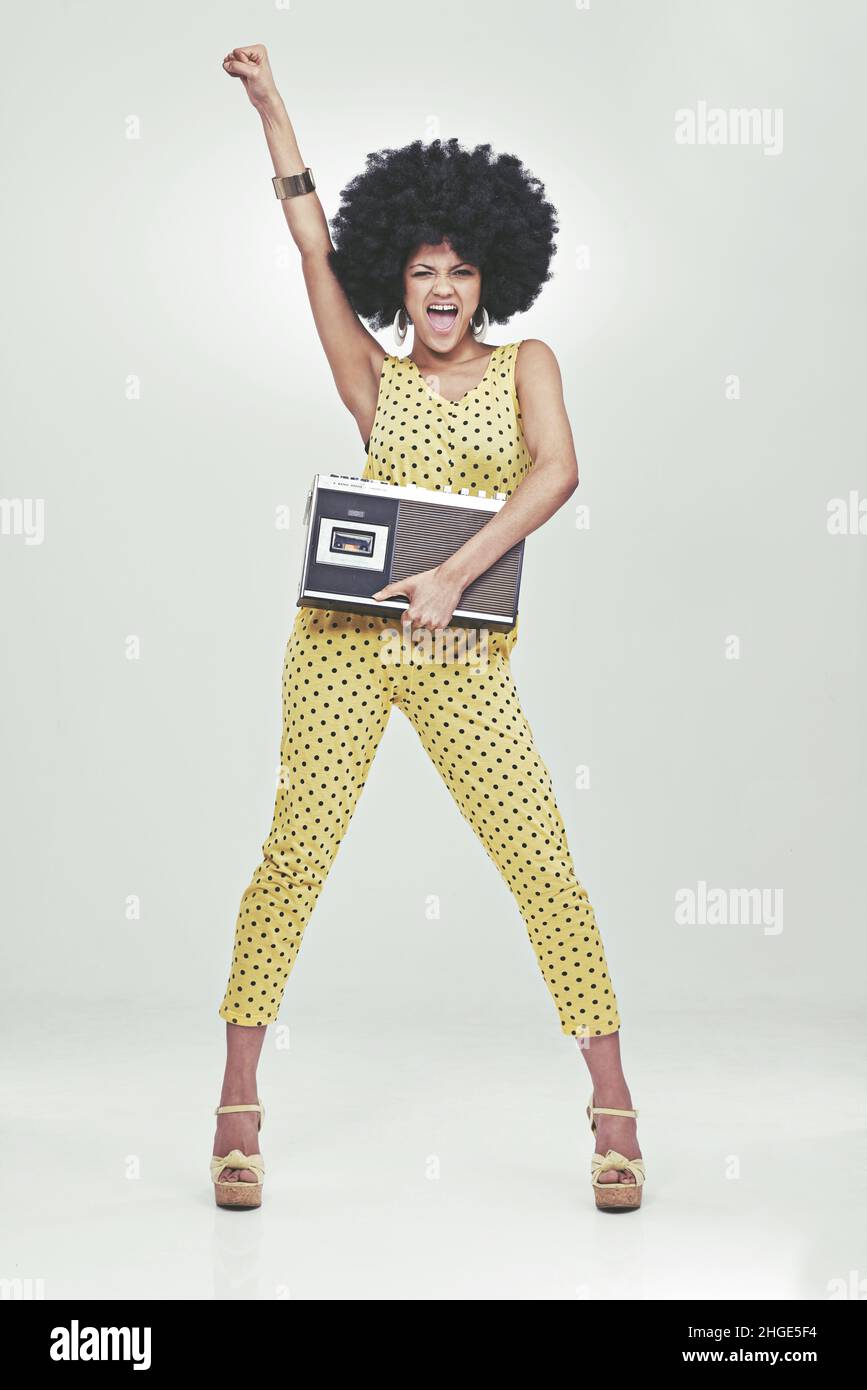 Il est temps de faire la fête - style 70s.Une jeune femme portant une combinaison rétro 70s tenant un lecteur de cassettes et frappant une pose disco. Banque D'Images