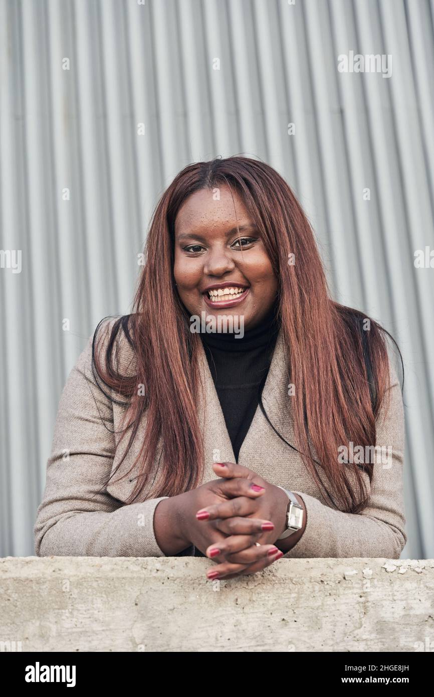 portrait de la jeune femme afro-américaine en costume avec de longs cheveux regardant l'appareil photo avec ses mains sur un mur. Banque D'Images