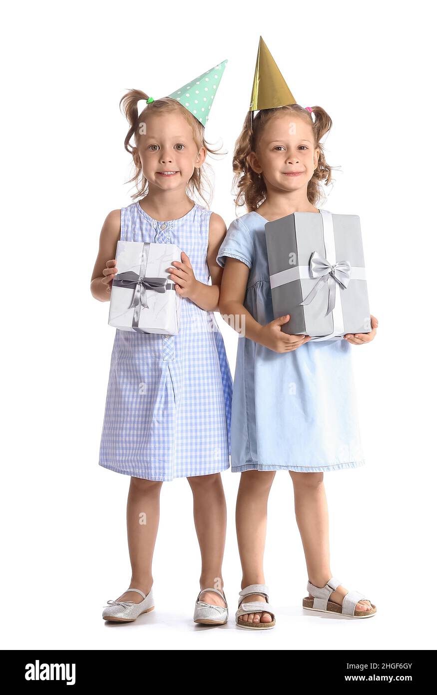 Petites filles drôles dans des chapeaux de fête avec des boîtes-cadeaux sur fond blanc Banque D'Images
