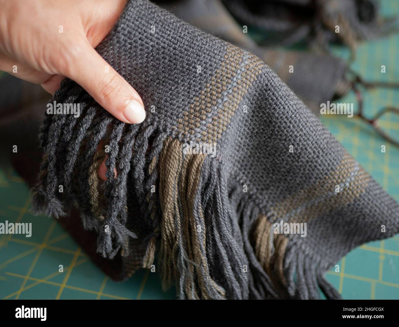 Main tenant un tissu tissé foncé avec une frange en fil de laine.Projet de tissage, mise au point sélective Banque D'Images