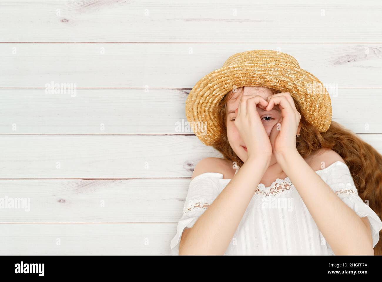 Jeune fille faisant un symbole de coeur avec ses mains, allongé sur un plancher en bois.Amour, amis, concept médical. Banque D'Images