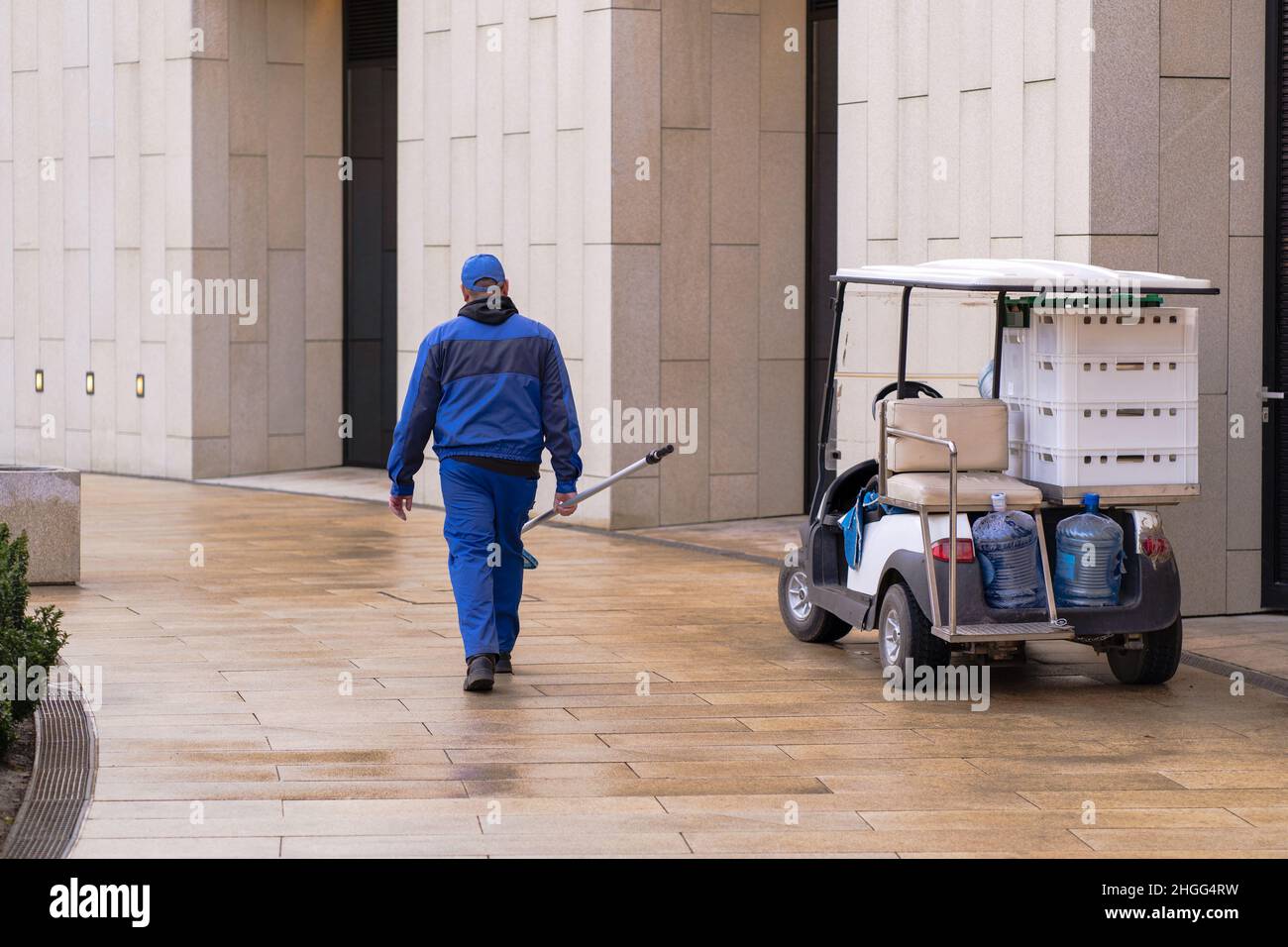 Homme, travailleur de parc vêtu d'un uniforme de travail bleu avec un filet pour enlever les feuilles de la piscine.Véhicule électrique ou voiture de golf. Banque D'Images