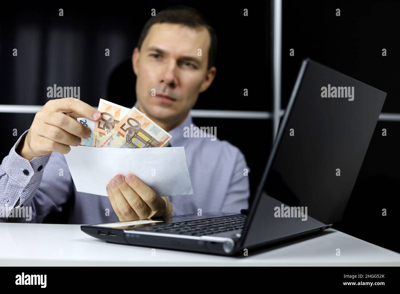 Enveloppe avec des billets en euros entre les mains de l'homme dans les vêtements de bureau assis à l'ordinateur portable.Concept de salaire, de prime ou de pot-de-vin Banque D'Images