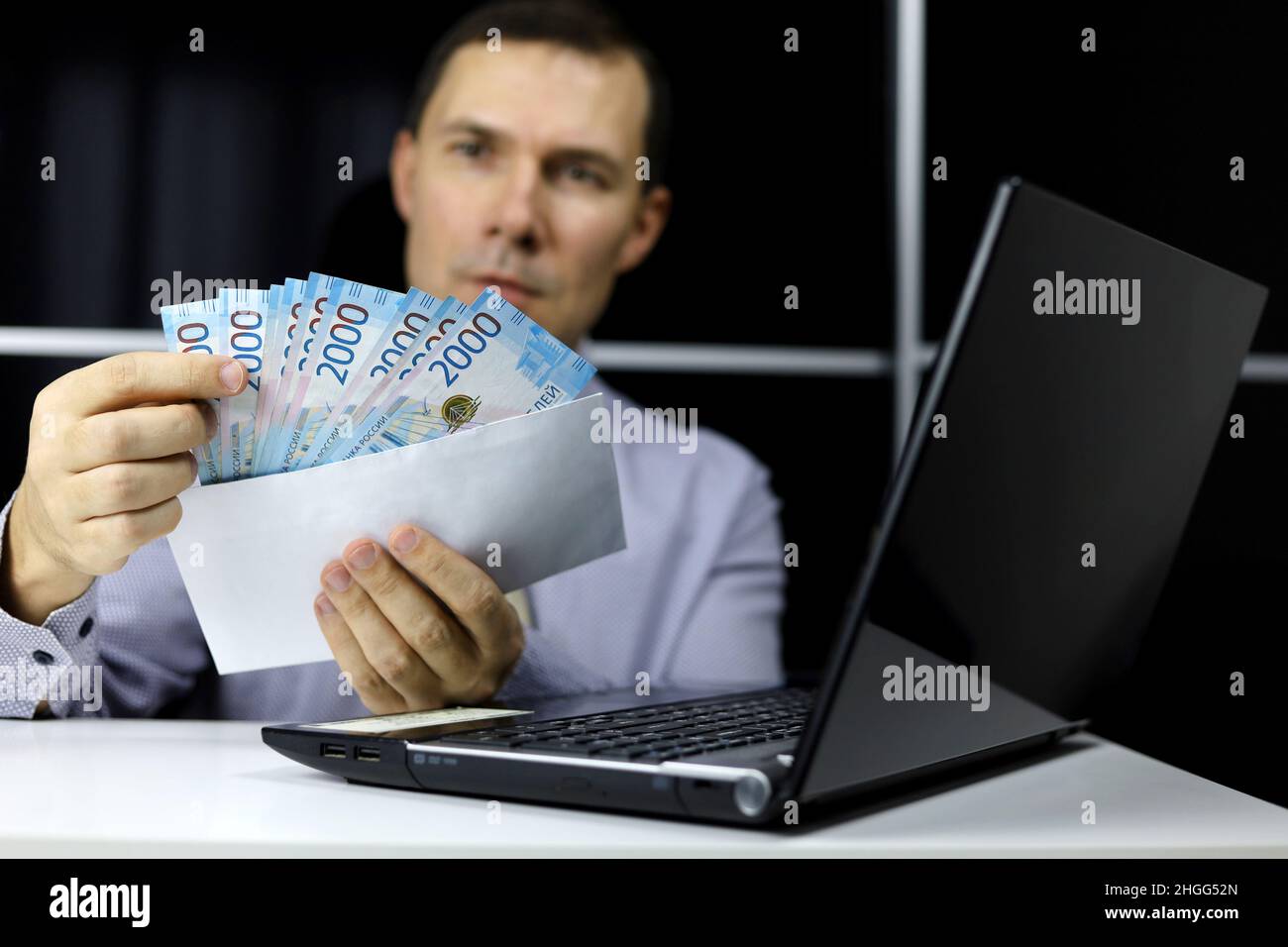 Enveloppe avec des roubles russes dans les mains de l'homme dans les vêtements de bureau assis à l'ordinateur portable.Salaires en Russie, concept de bonus ou de pot-de-vin Banque D'Images