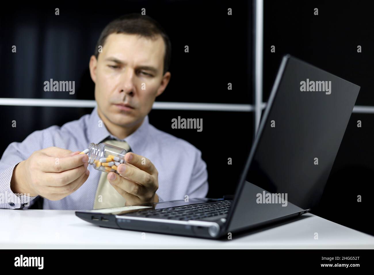 Pilules dans les mains de l'homme dans les vêtements de bureau assis à l'écran d'ordinateur portable.Médicaments en capsules, concept de prendre des médicaments au travail, antidépresseurs, maux de tête Banque D'Images