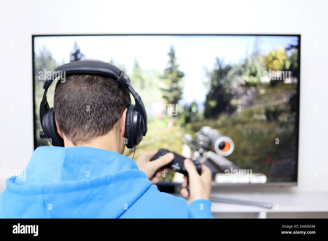 Guy dans les écouteurs jouant avec un jeu vidéo de jeu de tir de manette sur l'écran de TV.Concept de dépendance de jeu, loisirs à la maison Banque D'Images