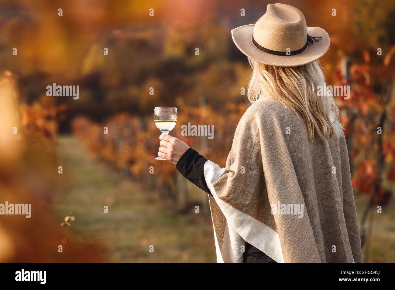 Femelle vigneron appréciant le vin blanc dans son vignoble.Femme avec poncho et chapeau tenant un verre de vin à l'extérieur.Cave de vinification à l'automne Banque D'Images