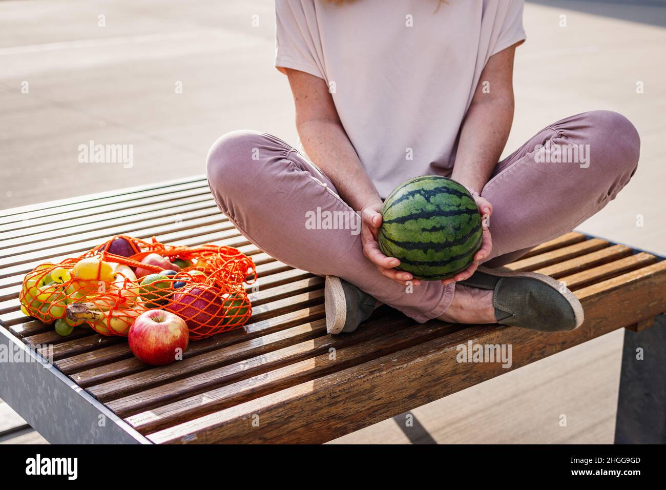 Femme tenant la pastèque et assise sur le banc en ville.Se reposer au banc après avoir fait des achats de fruits au supermarché.Concept zéro déchet et sans plastique Banque D'Images