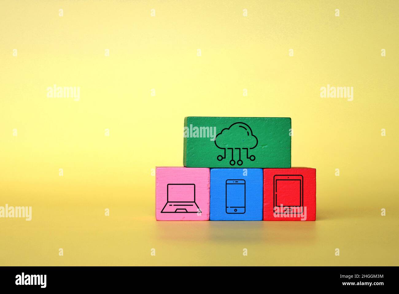 Concept de technologie et de cloud computing.Cubes en bois avec ordinateur portable, smartphone, tablette et icône de nuage sur fond jaune. Banque D'Images
