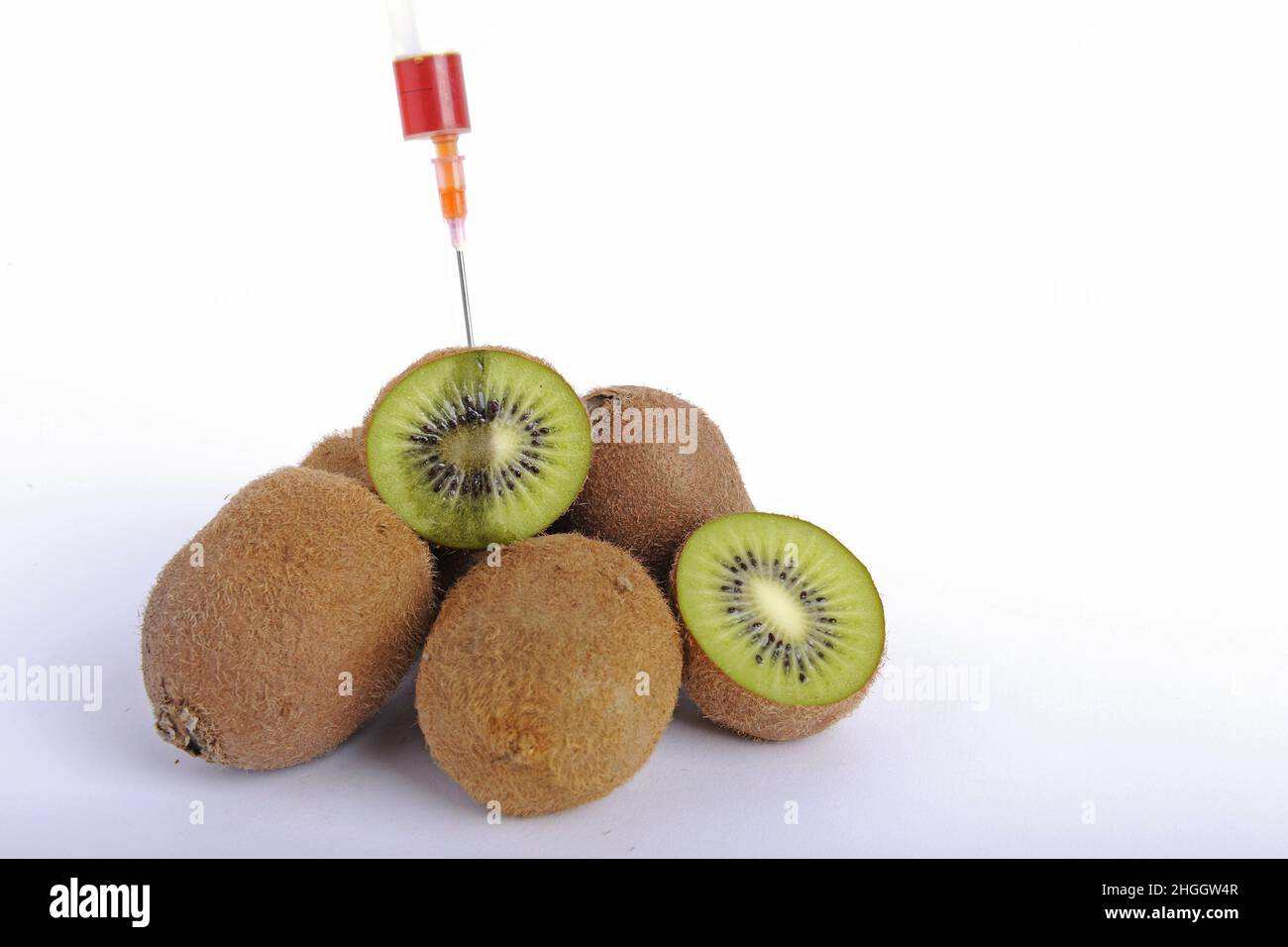 Kiwi, groseille chinoise (Actinidia Deliciosa), kiwis frais, en partie divisé par deux, seringue bloquée dans le kiwi, fruit génétiquement modifié Banque D'Images