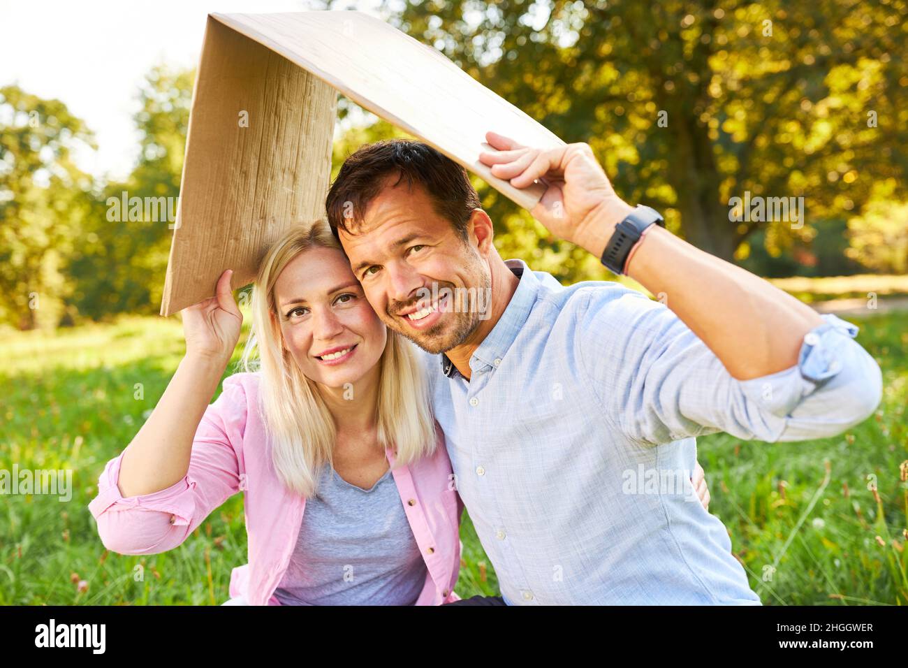 Un jeune couple heureux dans un parc avec un toit au-dessus de la tête symbolisant la propriété et la sécurité de la maison Banque D'Images