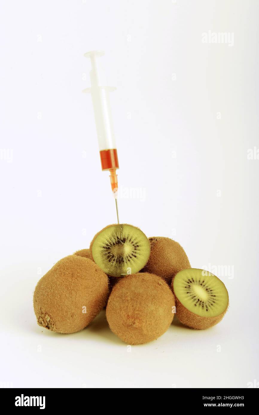 Kiwi, groseille chinoise (Actinidia Deliciosa), kiwis frais, en partie divisé par deux, seringue bloquée dans le kiwi, fruit génétiquement modifié Banque D'Images