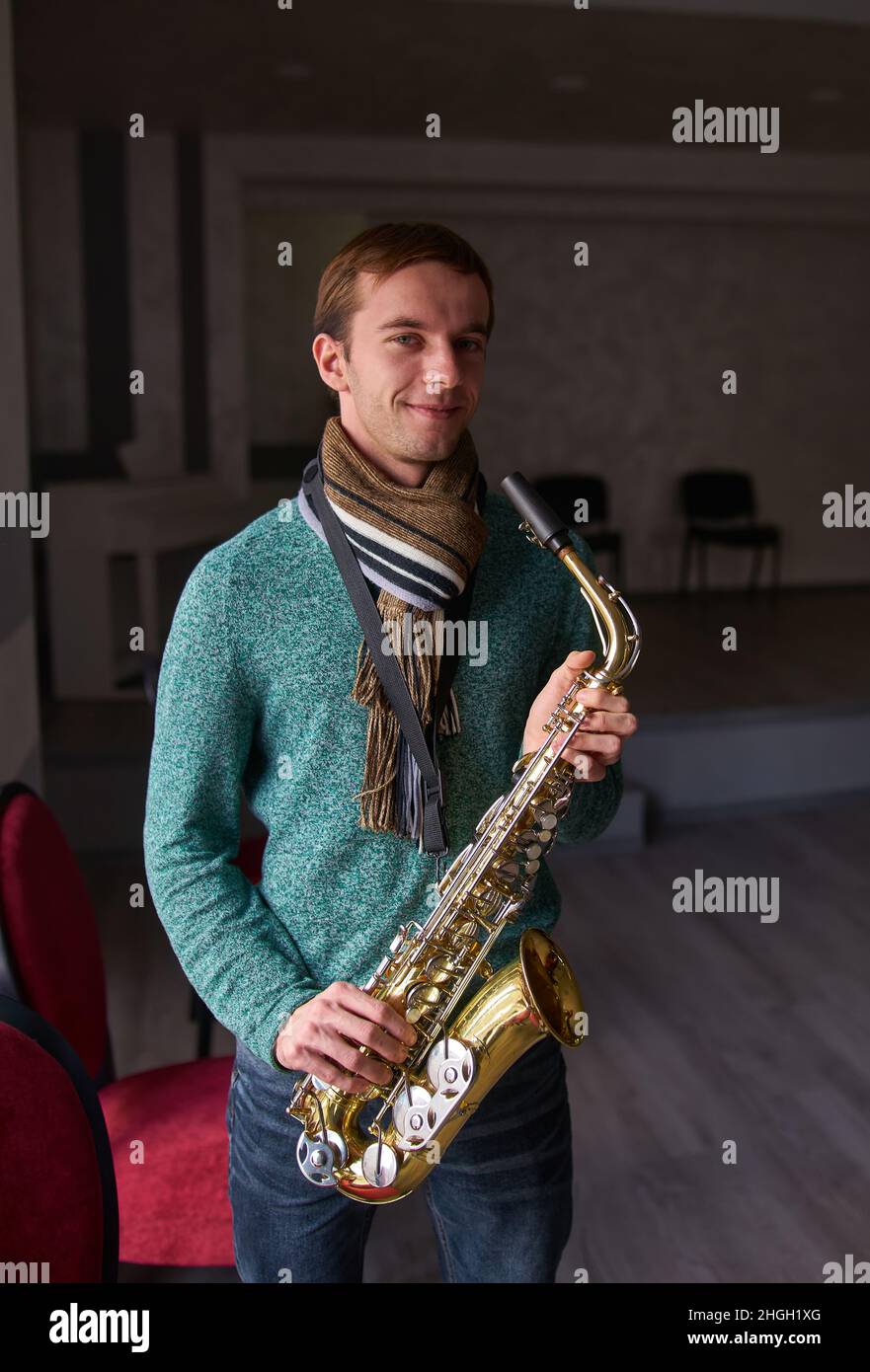 Jeune artiste de musique jazzman tenant un saxophone dans ses mains.La salle sombre de la salle de concert, éclairée par la lumière de la fenêtre Banque D'Images
