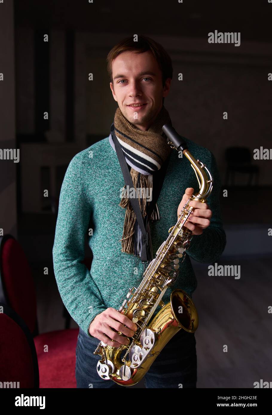 Jeune artiste de musique jazzman tenant un saxophone dans ses mains.La salle sombre de la salle de concert, éclairée par la lumière de la fenêtre Banque D'Images