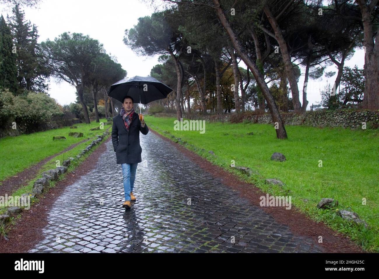 jeune homme italien élégant avec parapluie dans la pluie dans le parc Banque D'Images