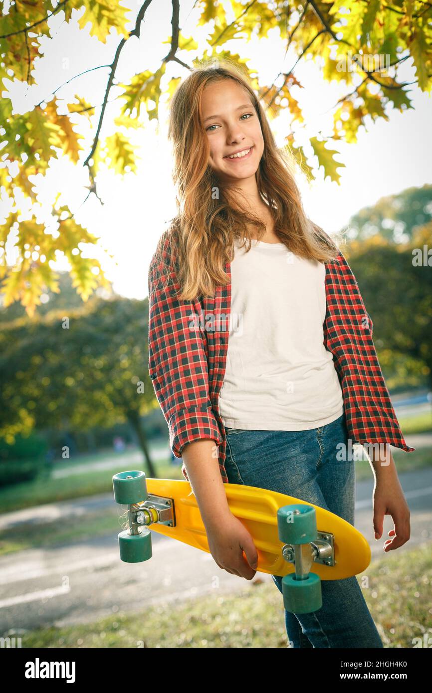 Portrait vertical de style de vie en plein air d'une jeune fille adolescente souriante avec un skateboard jaune portant une chemise à carreaux rouge Banque D'Images