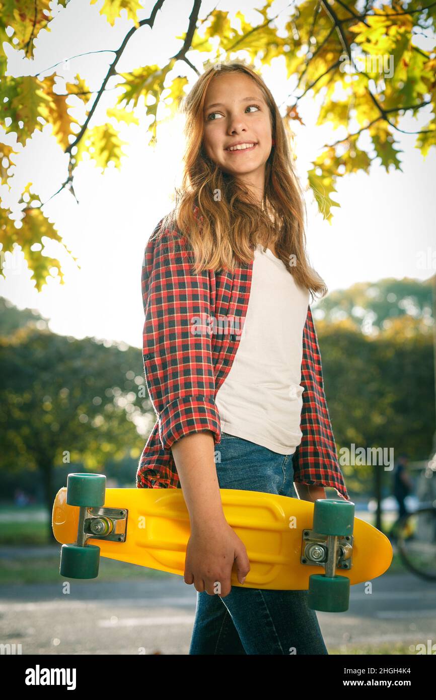 Portrait vertical de style de vie en plein air d'une jeune fille adolescente souriante avec un skateboard jaune portant une chemise à carreaux rouge Banque D'Images