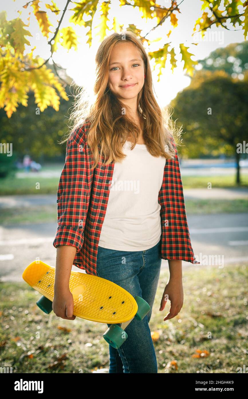 Portrait vertical de style de vie en plein air d'une jeune fille adolescente souriante avec un skateboard jaune portant une chemise à carreaux rouge Banque D'Images