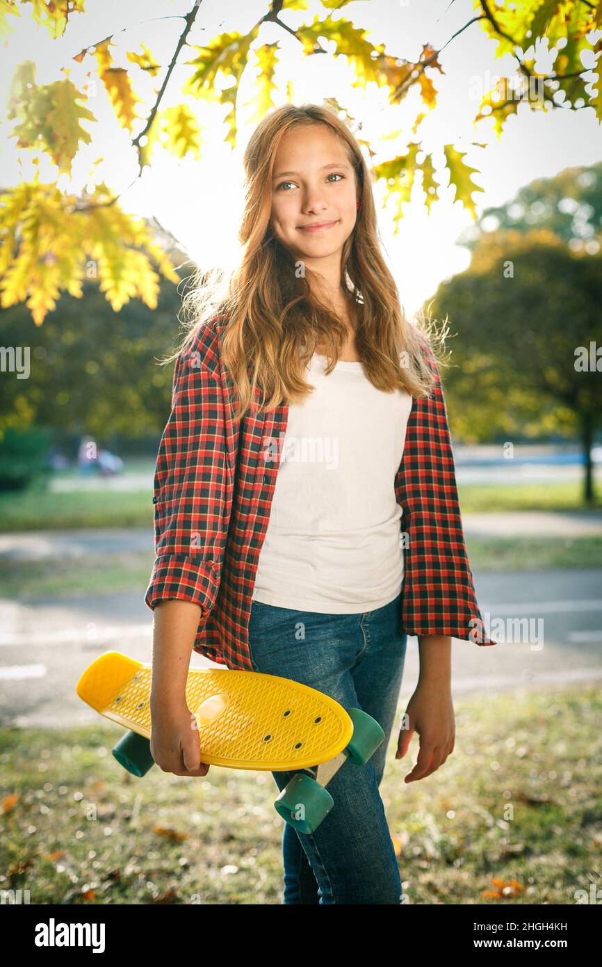 Portrait vertical de style de vie en plein air d'une jeune fille adolescente souriante avec un skateboard jaune portant une chemise à carreaux rouge Banque D'Images