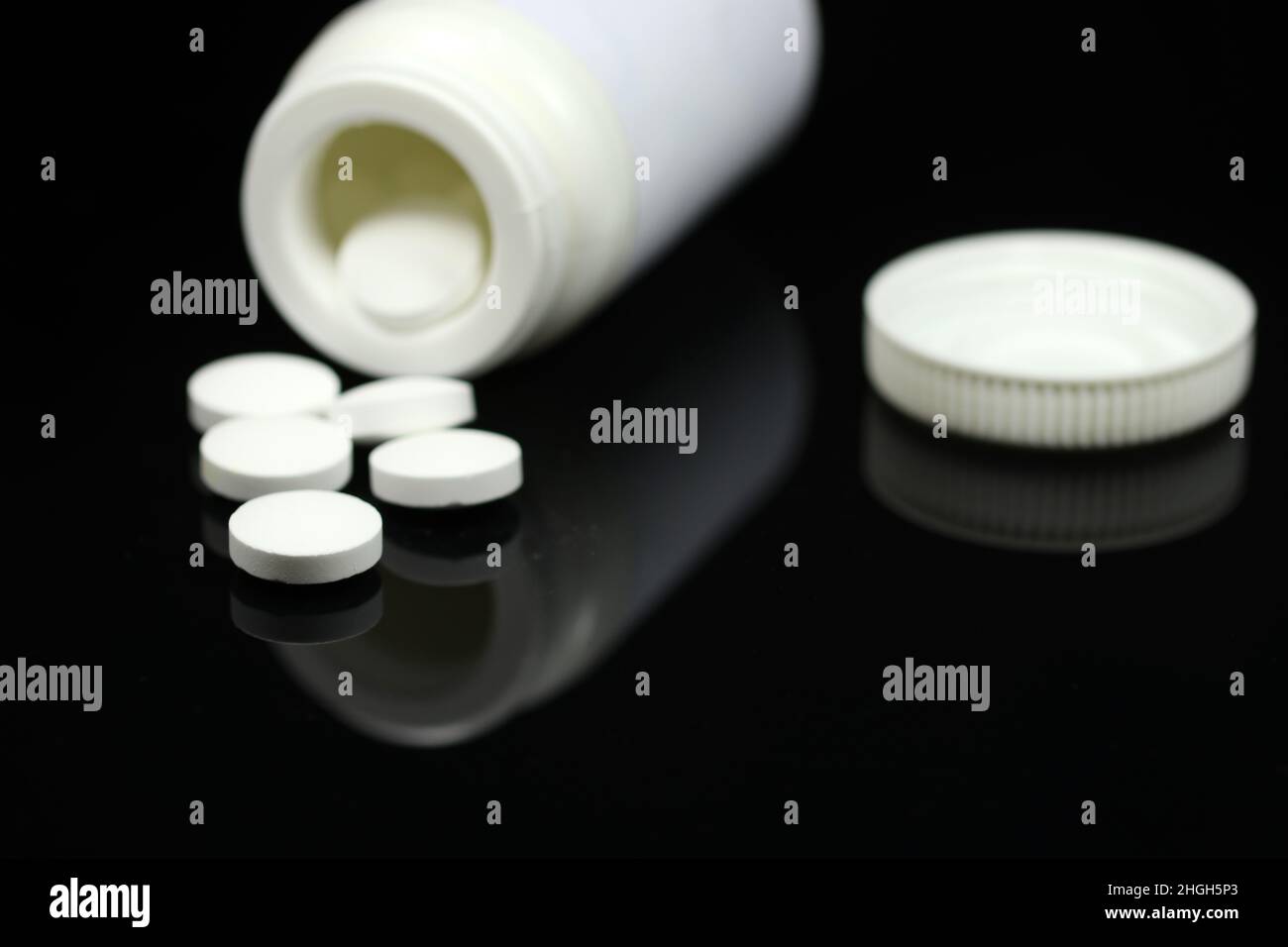 Comprimés et pilules médicaux blancs sortant d'une bouteille de médicament sur fond noir miroir.Arrière-plan flou.Vue macro avec espace de copie. Banque D'Images