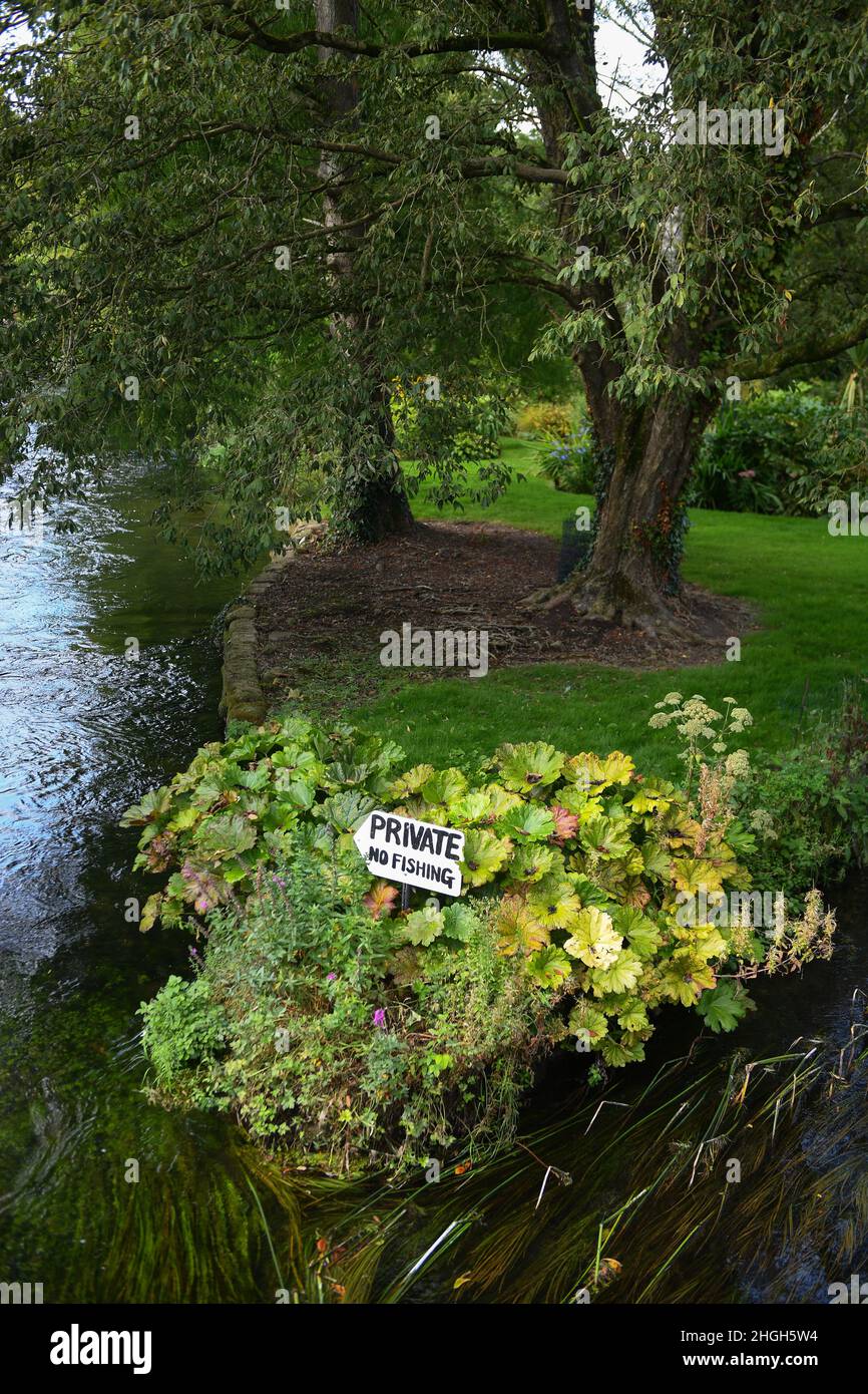 Un jardin privé rive de rivière en face d'un pont public sans panneau de pêche sur la rivière Test en cours d'exécution à travers la ville de marché de Romsey. Banque D'Images