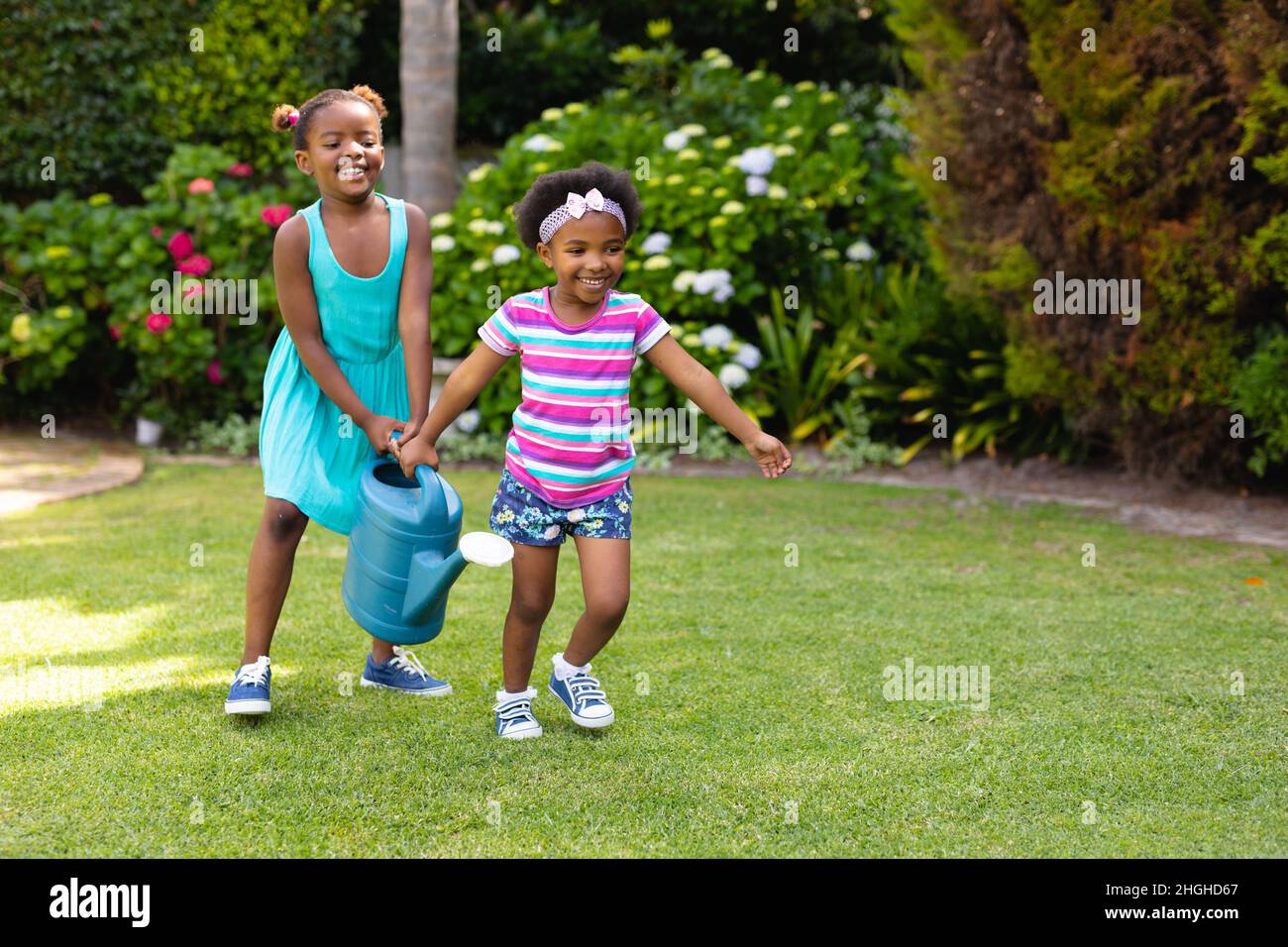 Deux sœurs afro-américaines avec arrosoir peuvent courir dans le jardin Banque D'Images