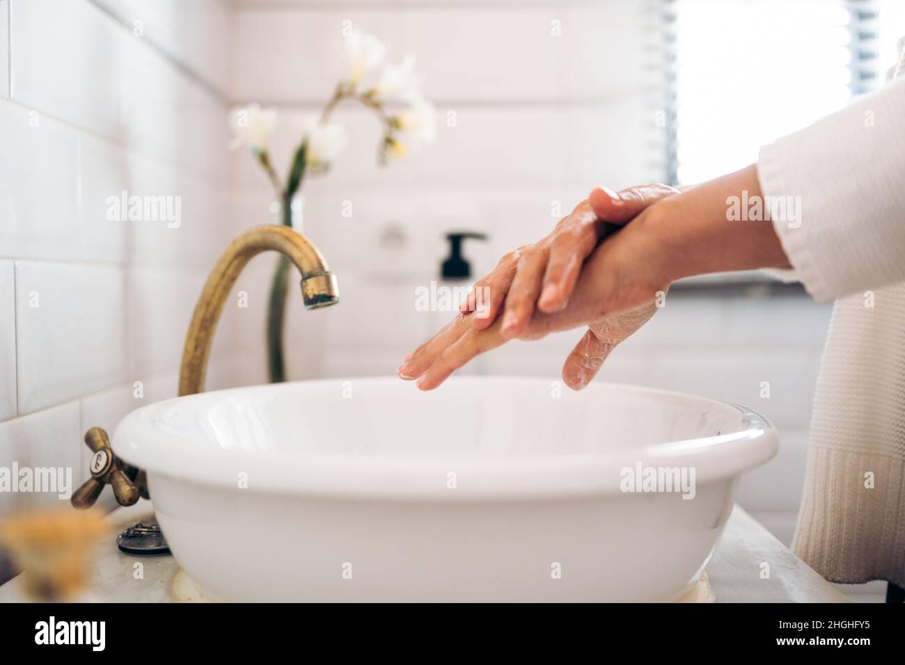 Une femme méconnaissable se lavant les mains avec du savon dans une salle de bain Banque D'Images