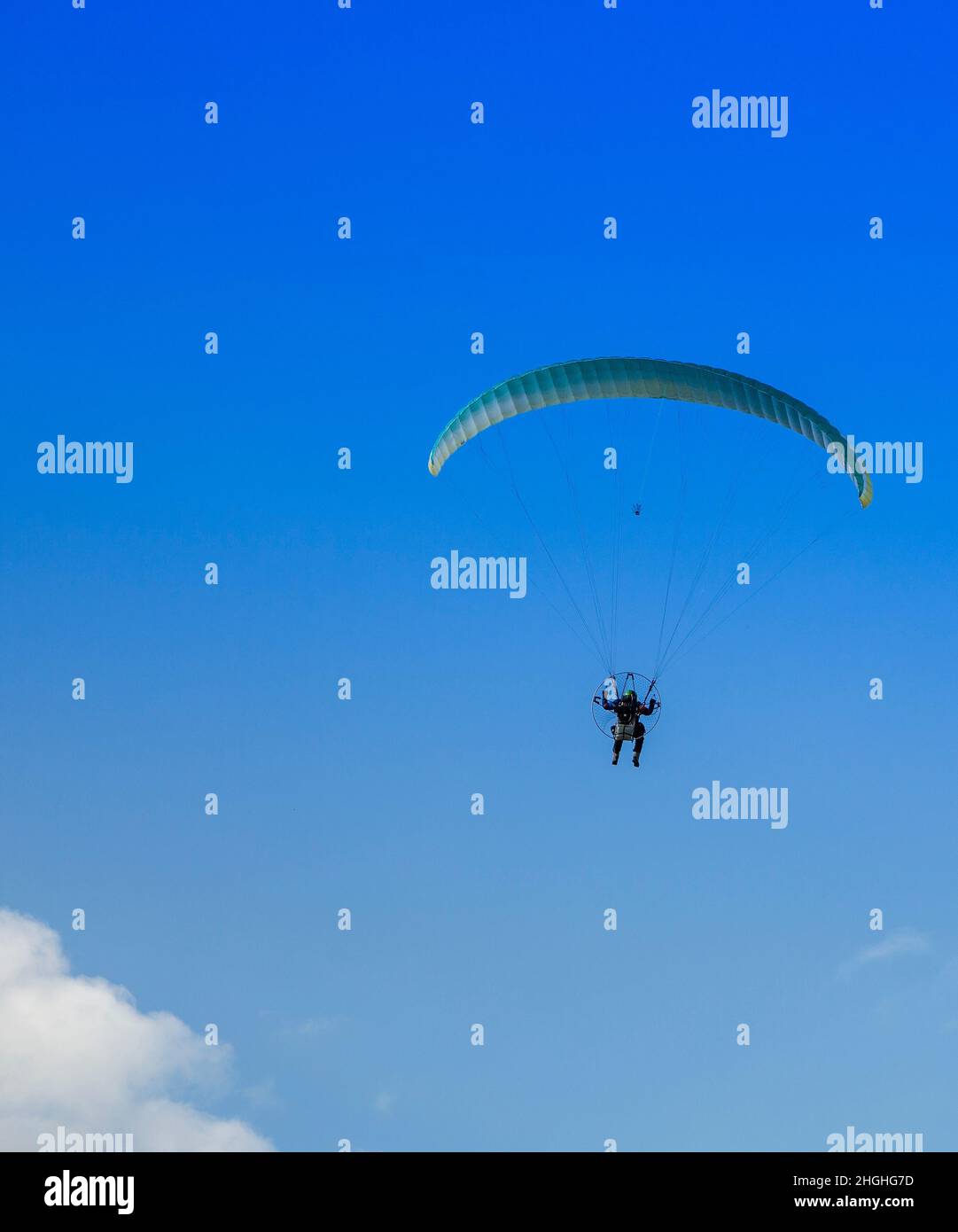 Un homme avec un parapente jaune et un petit moteur volant sur un ciel bleu par une journée ensoleillée. Banque D'Images