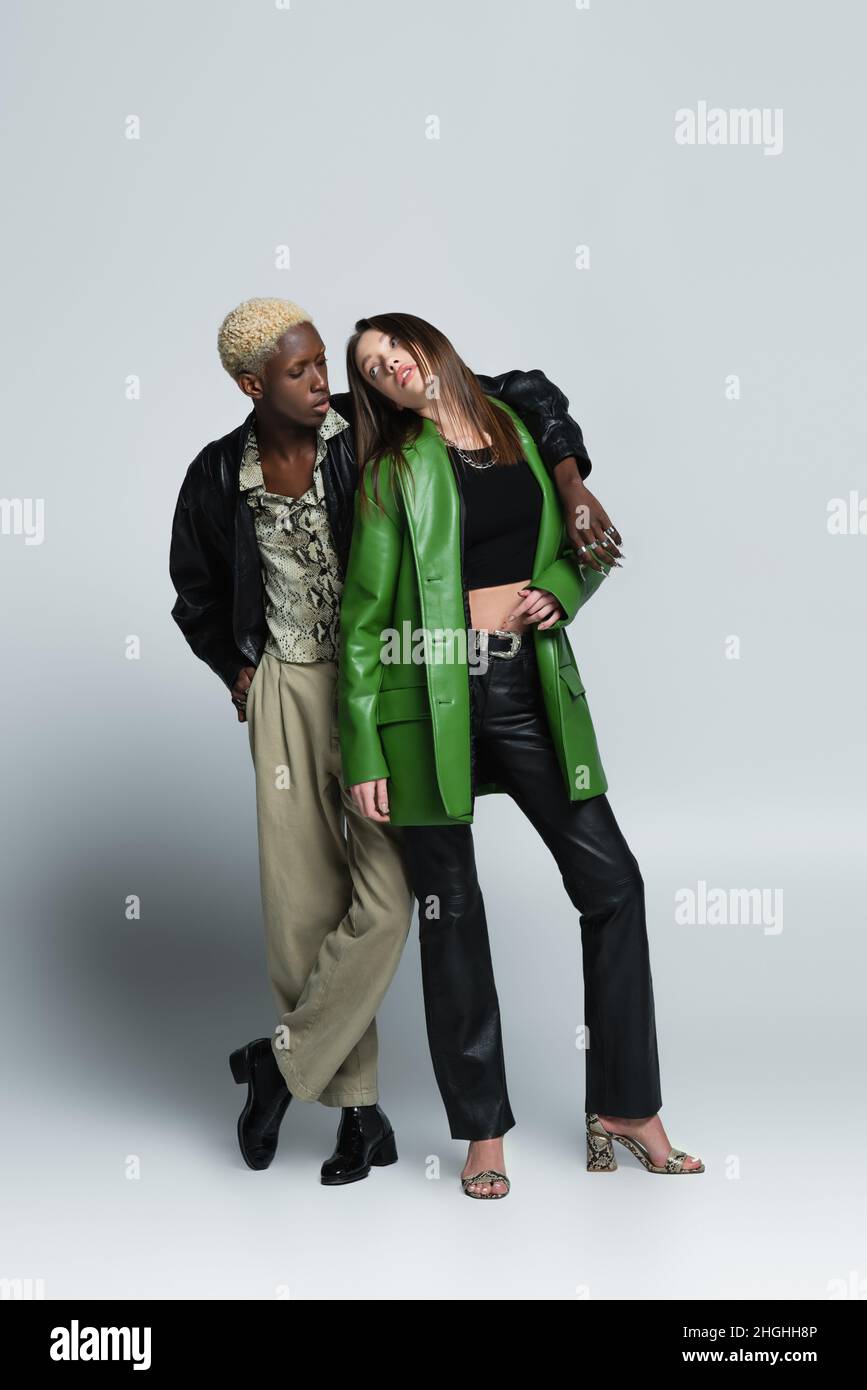 homme améican africain blond embrassant la femme brune en cuir vert veste sur gris Banque D'Images