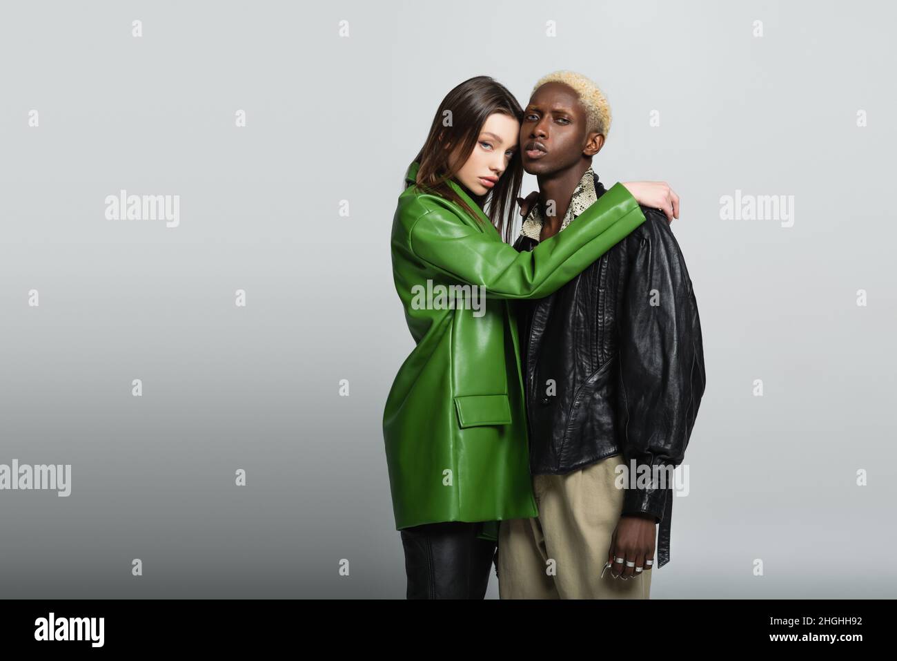 jolie femme en cuir vert veste embrassant l'homme afro-américain élégant sur le gris Banque D'Images