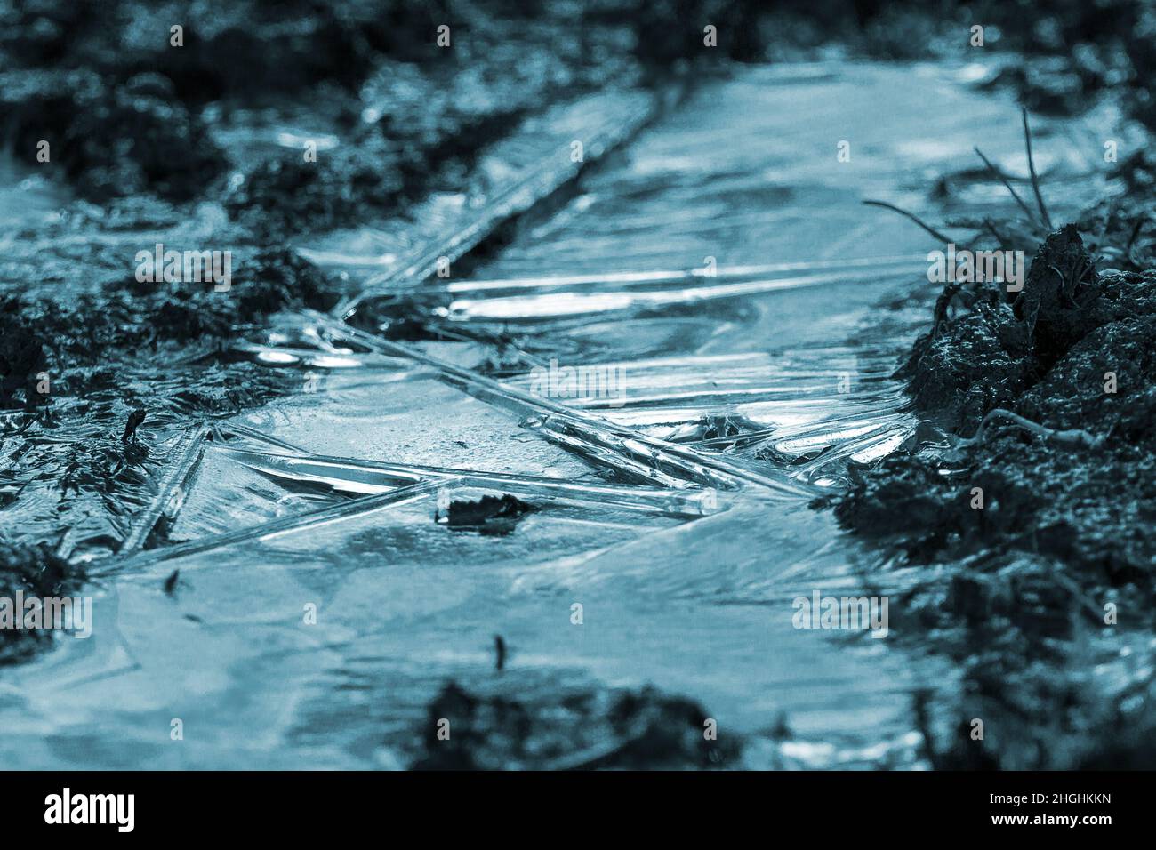 Glace sur fond de boue gelé teinte bleu monochrome format paysage.Lignes inclinées dures dans les zones lisses de glace et sol partiellement gelé.Textures d'arrière-plan ou image de glace Banque D'Images