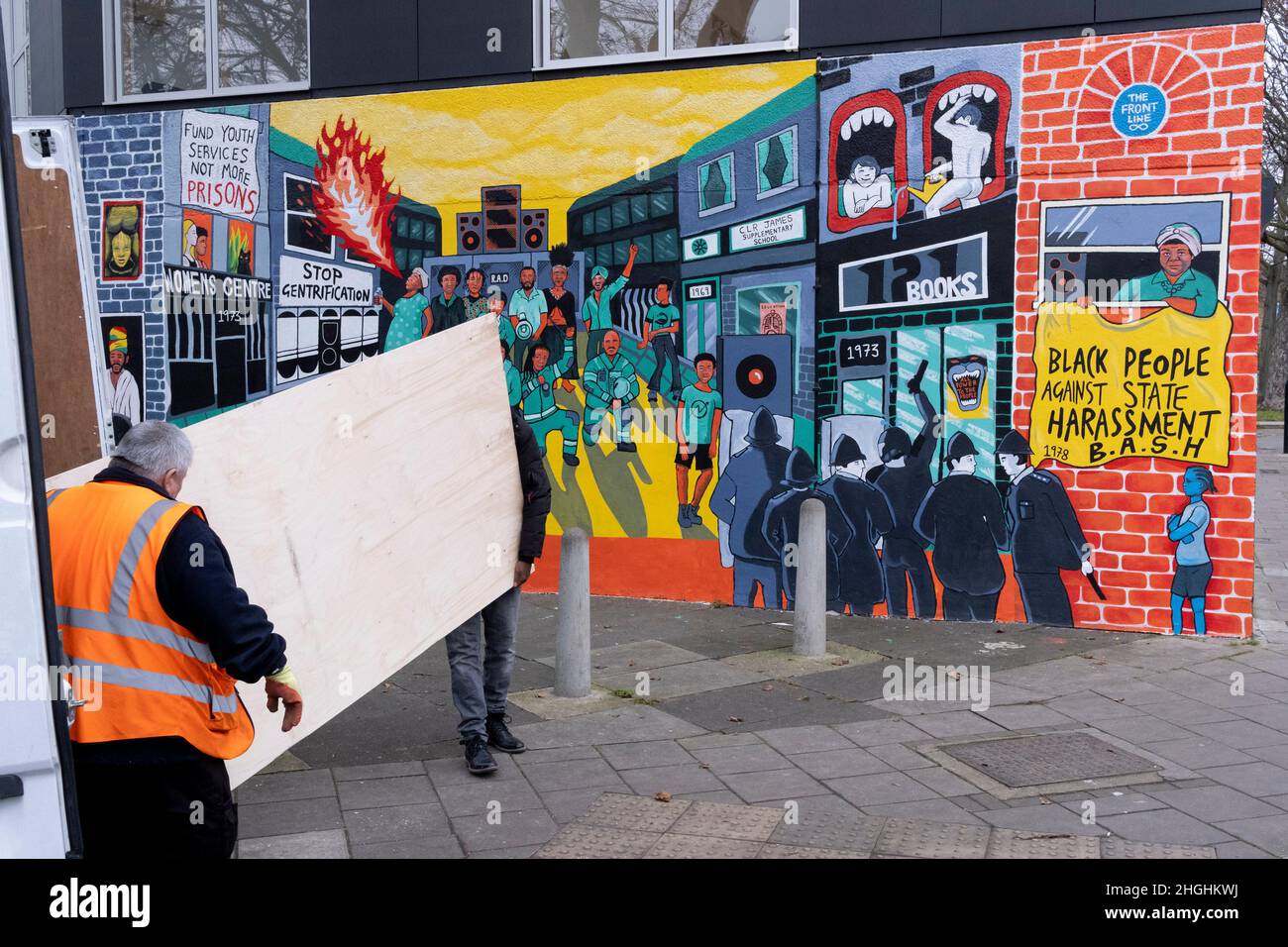 Deux hommes transportent des fournitures d'une camionnette blanche et ont passé une fresque qui rappelle les émeutes de Brixton en 1981 et le racisme systématique et le harcèlement par la police de la communauté noire de Brixton, le 21st janvier 2022, à Railton Road, Londres, Angleterre.L'œuvre, des artistes Jacob V Joyce, Monique Jackson, Ailsa Yexley, Buki Bayode et Sola Olulode, a été financée par le couronnement et représente le 40th anniversaire des soulèvements de Brixton de 1981, lorsque les émeutes ont commencé les 10th, 11th et 12th avril 1981 sur le chemin Railton de Brixton, connu sous le nom de Front Line .(Légende complète dans informations supplémentaires). Banque D'Images