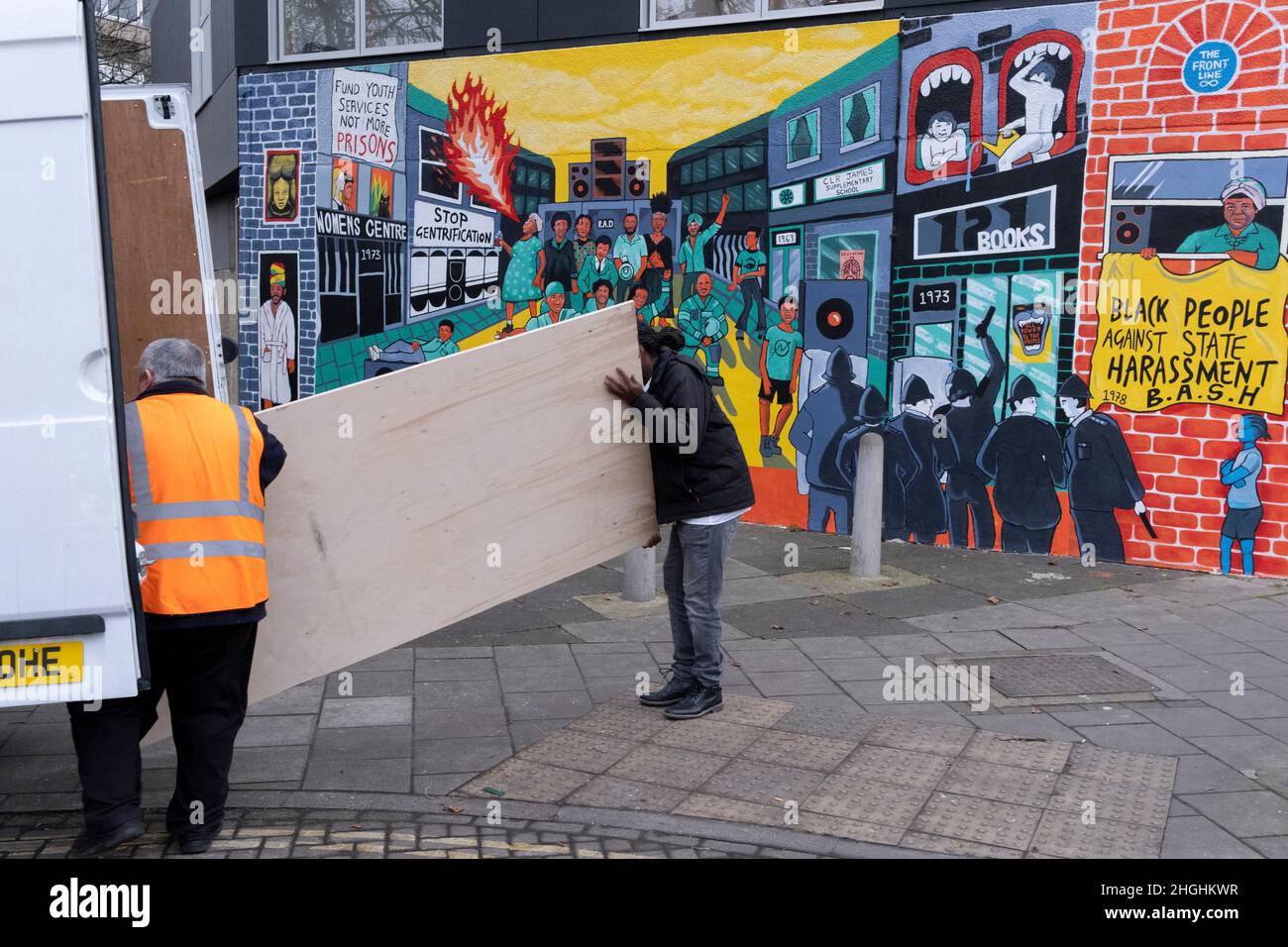 Deux hommes transportent des fournitures d'une camionnette blanche et ont passé une fresque qui rappelle les émeutes de Brixton en 1981 et le racisme systématique et le harcèlement par la police de la communauté noire de Brixton, le 21st janvier 2022, à Railton Road, Londres, Angleterre.L'œuvre, des artistes Jacob V Joyce, Monique Jackson, Ailsa Yexley, Buki Bayode et Sola Olulode, a été financée par le couronnement et représente le 40th anniversaire des soulèvements de Brixton de 1981, lorsque les émeutes ont commencé les 10th, 11th et 12th avril 1981 sur le chemin Railton de Brixton, connu sous le nom de Front Line .(Légende complète dans informations supplémentaires). Banque D'Images