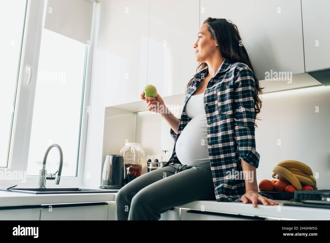 Femme enceinte mangeant de la pomme tout en préparant de la salade de légumes dans la cuisine à la maison Banque D'Images