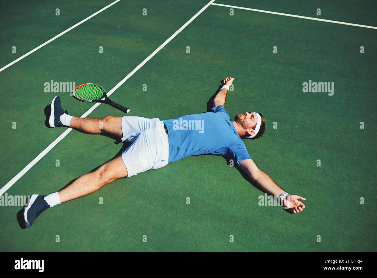 La victoire se sent si bonne.Photo en plein air d'un jeune homme de tennis beau allongé sur un court de tennis. Banque D'Images