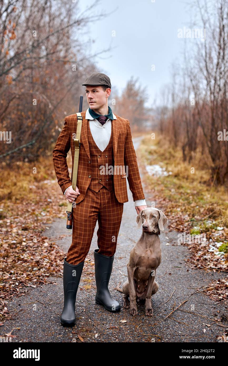 magnifique chien de chasse gris avec propriétaire pendant une journée de chasse.Saison d'automne, chasseur. Plein air. Jeune caucasien fort mâle dans la tendance marron costume marche Banque D'Images