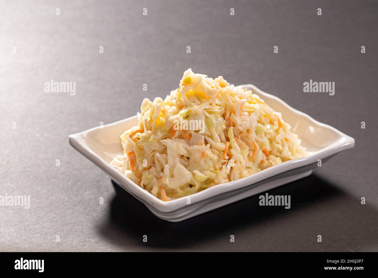 Salade fraîche crémeuse de coleslaw au chou et à la carotte servie dans un plateau blanc sur fond gris foncé vue du dessus Banque D'Images