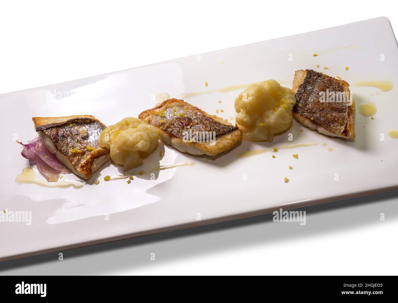 Filet de bar poêlé avec chou-fleur, oignon et zeste de citron râpé sur une assiette rectangulaire blanche Banque D'Images