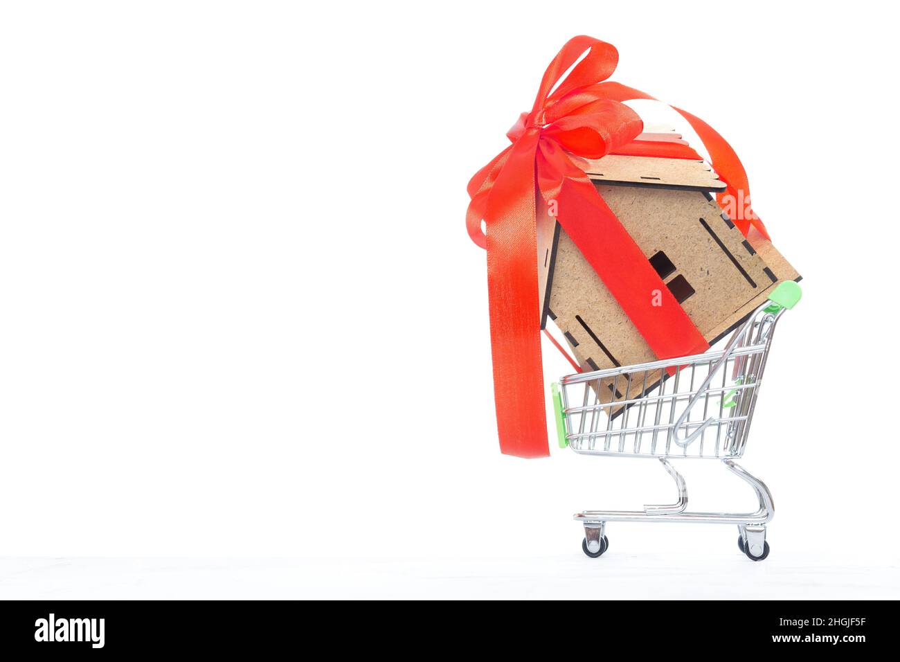 Petite maison de jouets décorée d'un ruban rouge et d'un noeud dans un petit panier isolé sur blanc.Le concept d'achat d'une maison. Banque D'Images