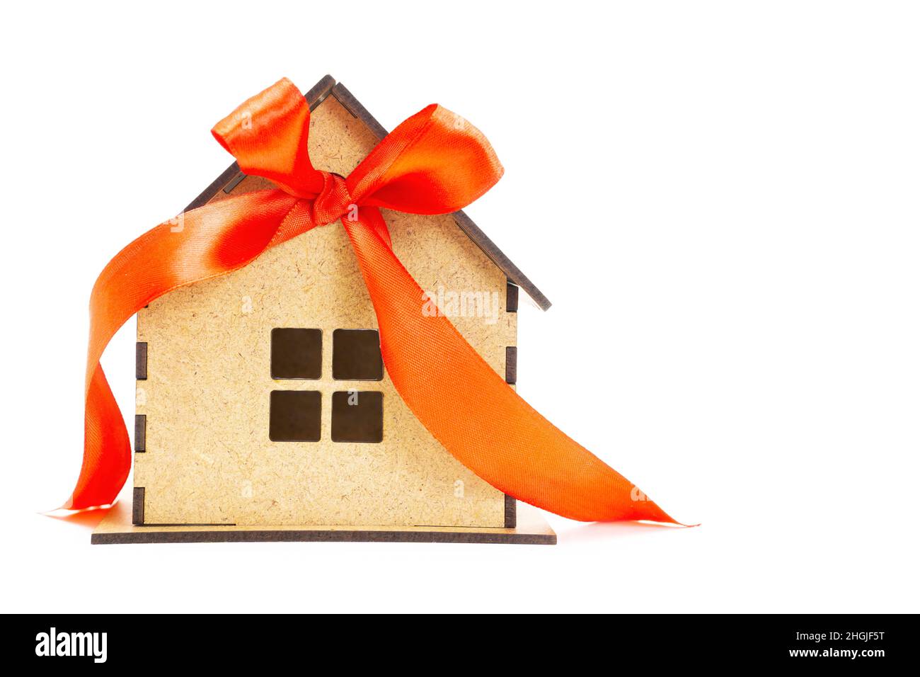 Maison miniature en bois décorée d'un ruban rouge et d'un noeud isolé sur fond blanc.Acheter une nouvelle maison. Banque D'Images