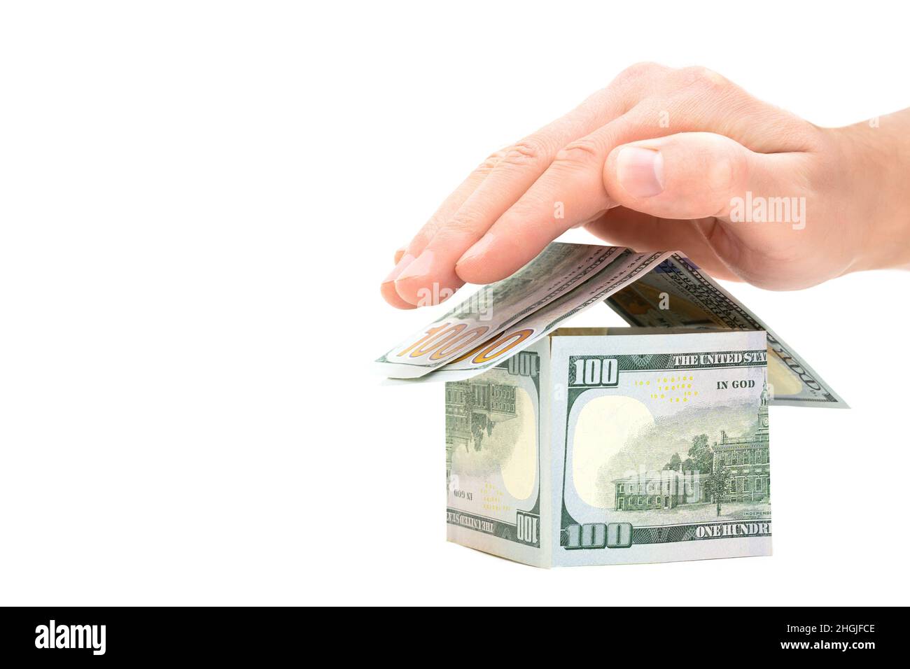 Main humaine couvrant un modèle de maison fait de cent billets de dollars isolés sur fond blanc.Concept créatif d'assurance immobilière. Banque D'Images