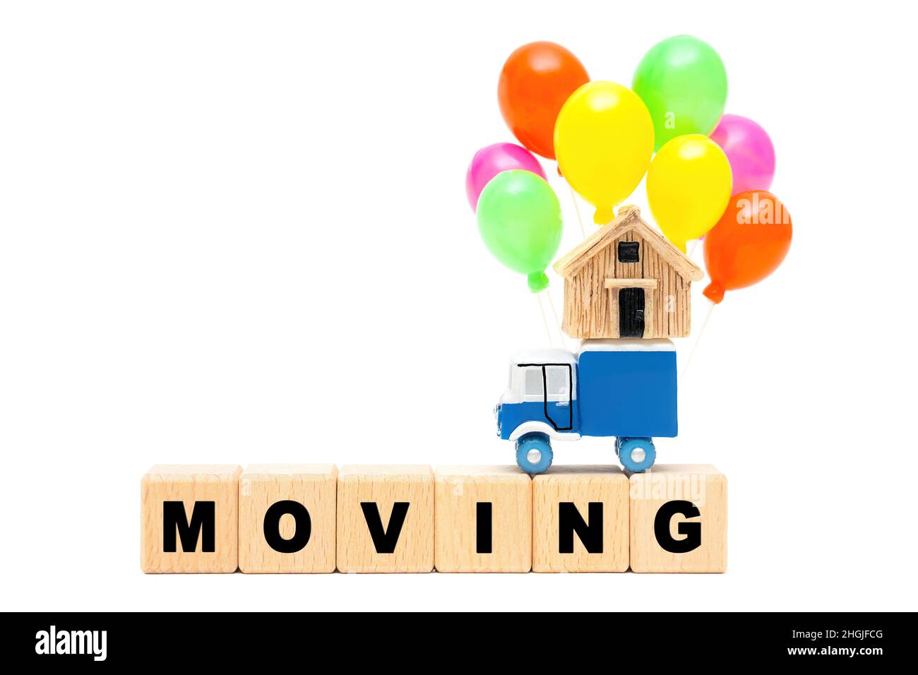 Camion de jouets transportant une maison miniature et un groupe de ballons de fête multicolores sur une rangée de blocs de lettres en bois se DÉPLAÇANT isolé sur la ba blanche Banque D'Images