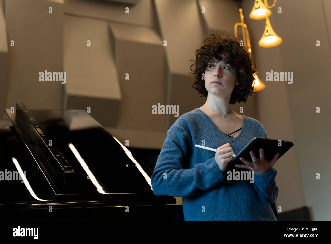 Jeune femme aux cheveux bouclés penchée contre un piano à queue en pensant à quoi écrire Banque D'Images