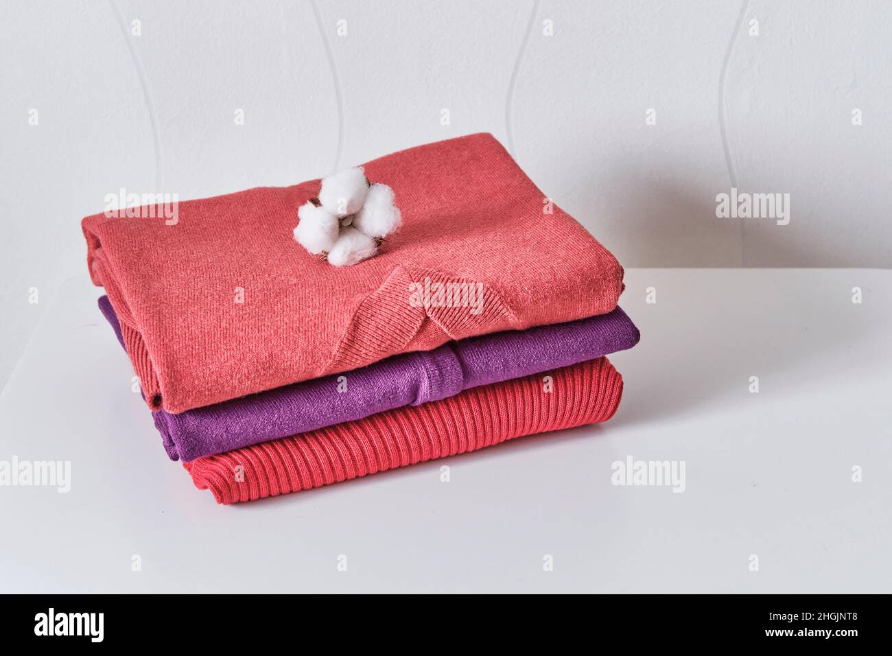 Vêtements féminins tricotés en corail, violet et rouge empilés soigneusement sur une table blanche. Banque D'Images