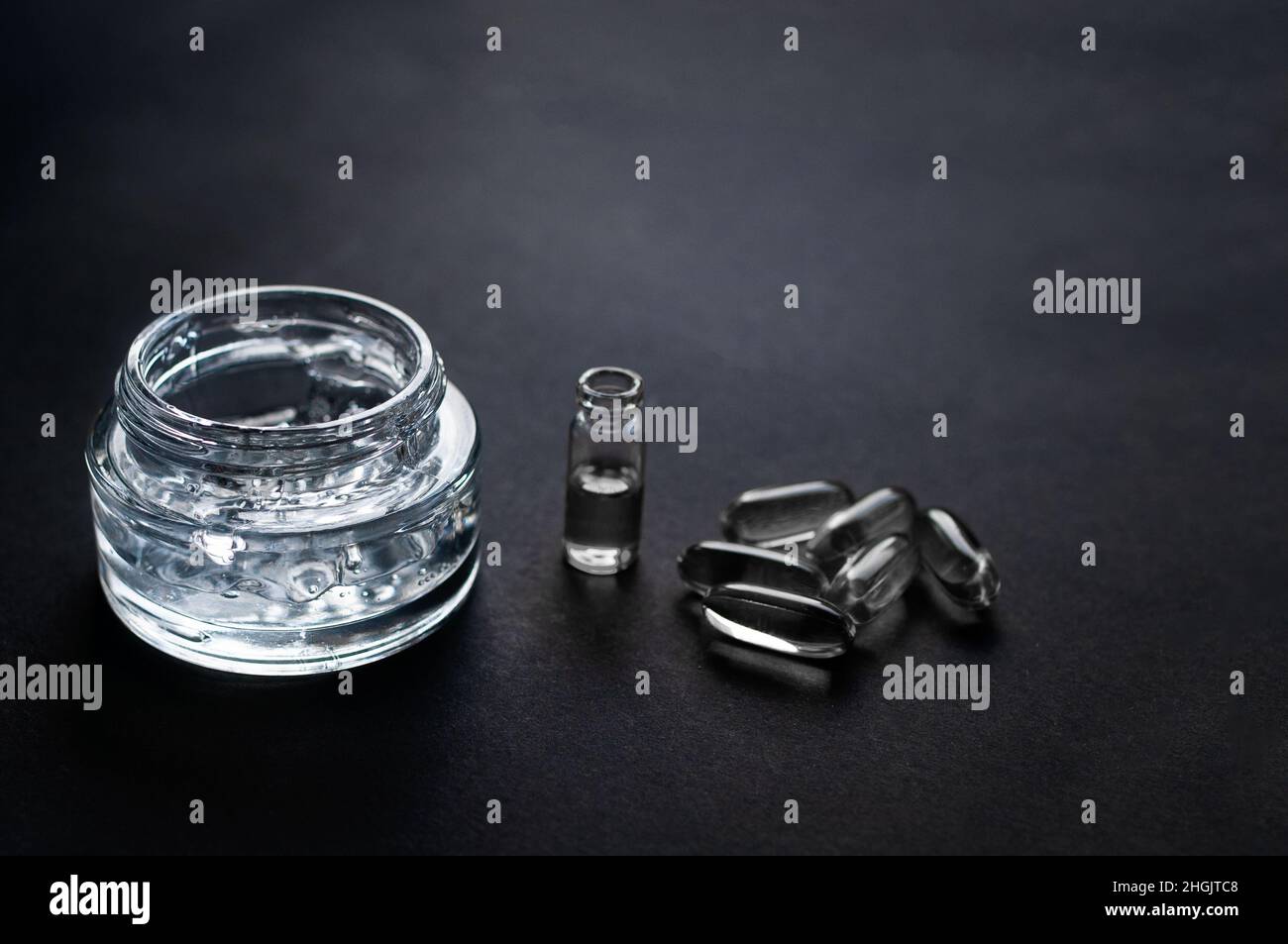 pot transparent avec gel hydratant avec acide hyaluronique et vitamines en capsules sur fond noir Banque D'Images