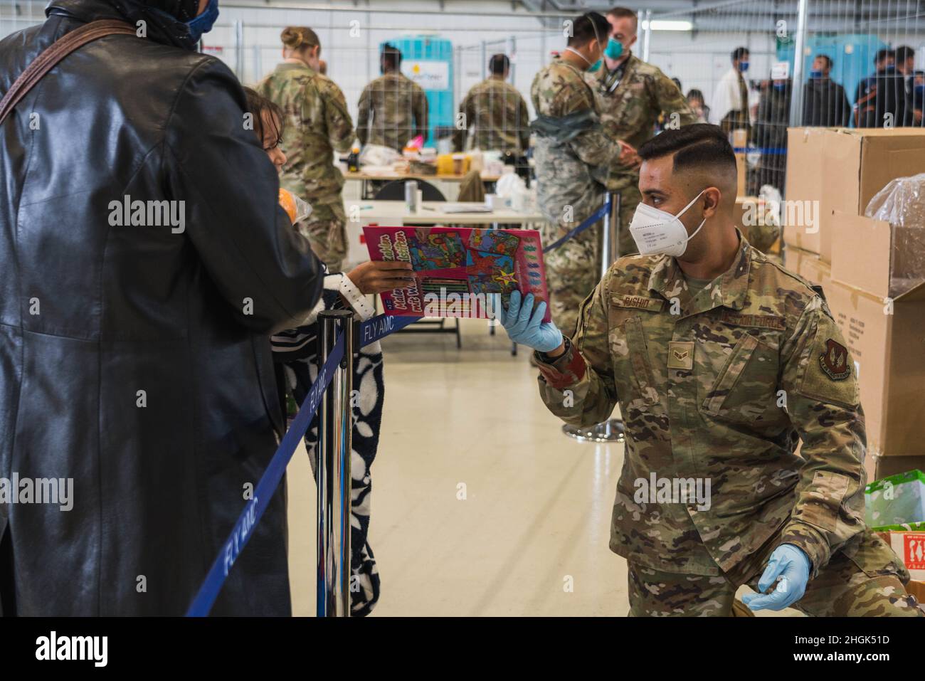 U.S. Air Force Airman classe 1st Sulieman Rashid, apprenti en gestion de véhicules de l'escadron de préparation logistique 52nd, remet un livre de coloriage à un enfant évacué à Hangar 5, à la base aérienne de Ramstein, en Allemagne, le 27 août 2021.L'escadre des opérations de mobilité aérienne de 521st a transformé l'un des plus grands hangars à Ramstein en un terminal passager supplémentaire pour soutenir l'opération alliés refuge. Banque D'Images