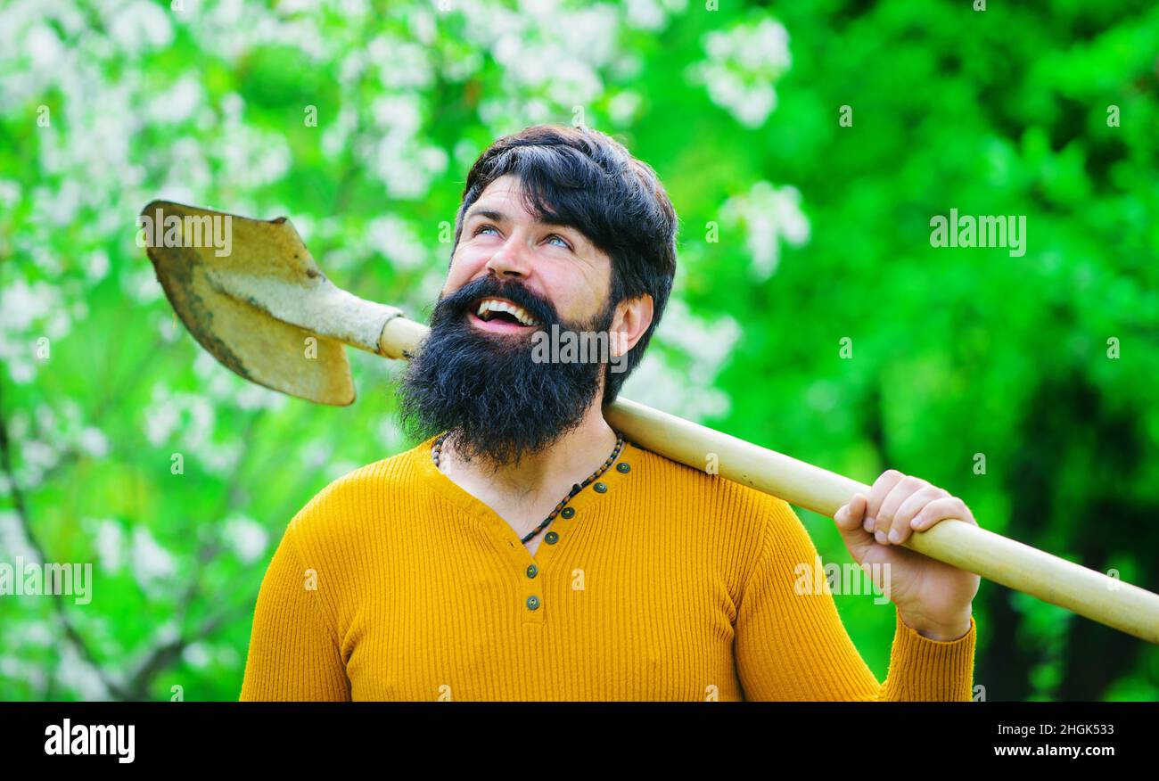 Jardinage.Homme heureux dans le jardin de printemps.Travaux de jardinier.Mâle barbu plantant avec une pelle.Éco-exploitation. Banque D'Images