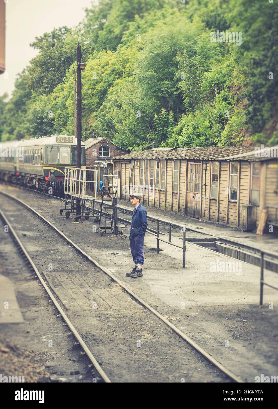 Homme bénévole debout dans des sidings à la gare du patrimoine britannique par des hangars sous le soleil d'été. Banque D'Images